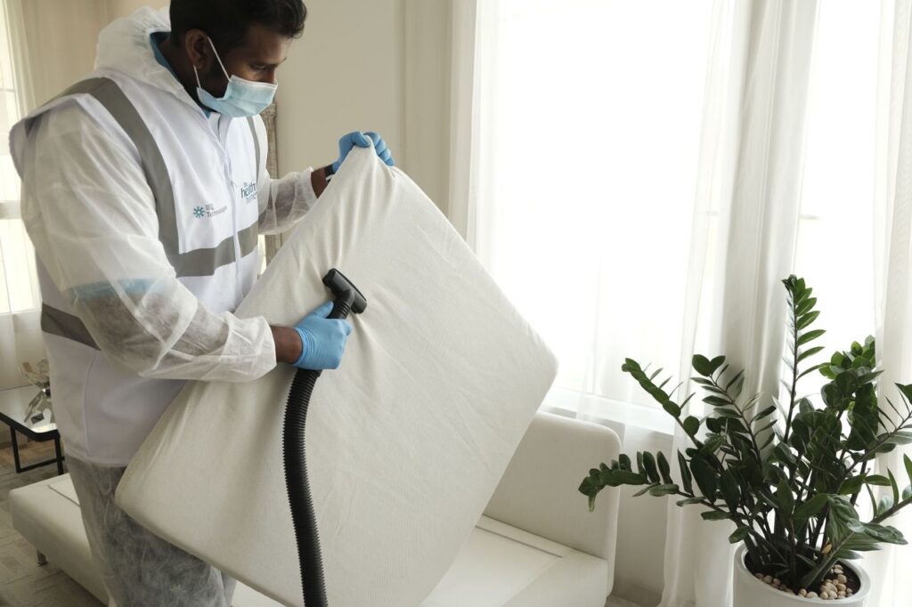 services-02 Man in protective gear vacuuming a mattress in a modern home interior.