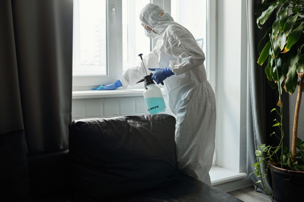 services-01 Person in PPE disinfecting indoor window area during COVID-19 pandemic.
